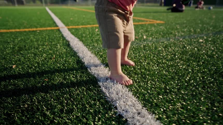 Little boy walking on artificial grass and falling