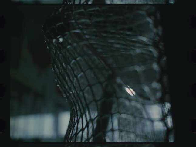 A close up of a puck hitting the net of a goal in a dimly lit ice hockey rink