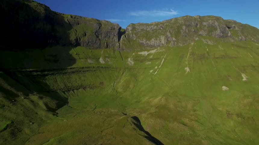 A view of a large hole surrounded by mountains and is covered in green