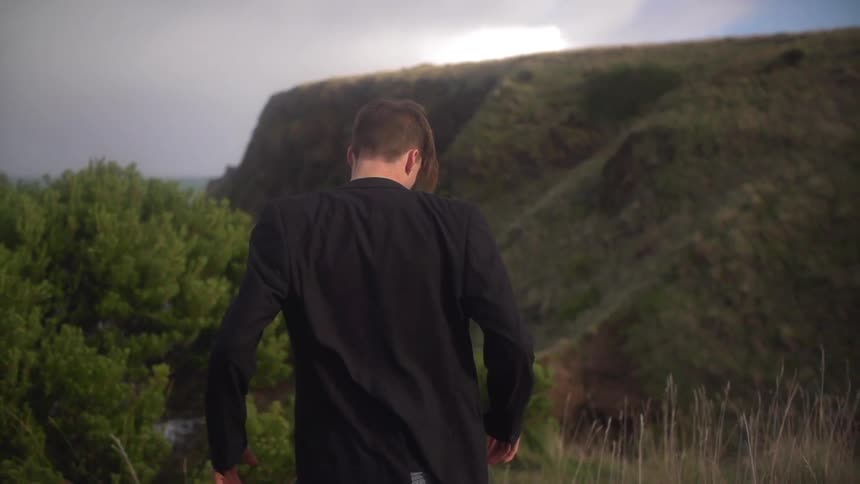 Man walking through a field towards a large hill by the shore