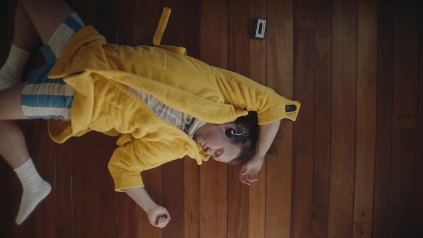 Person lying on a wooden floor wearing a yellow robe and headphones
