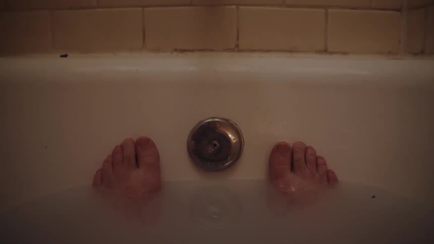 A persons feet inside a bathtub with the feet submerged in the water leaving the toes out