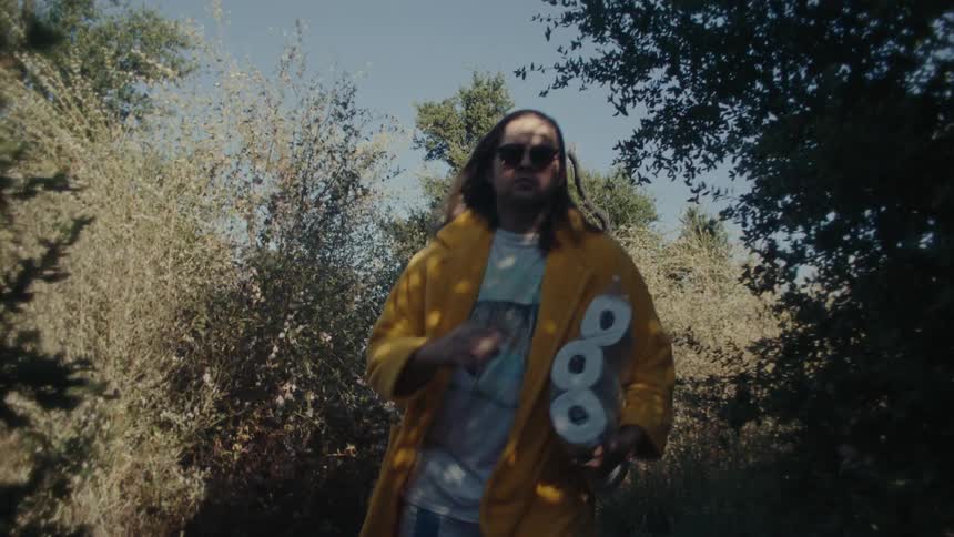 Man in sunglasses running down a trail during the day carrying a pack of toilet paper