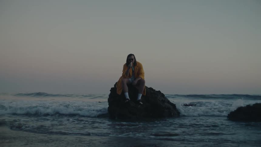 A man eats a banana while sitting on a seaside rock