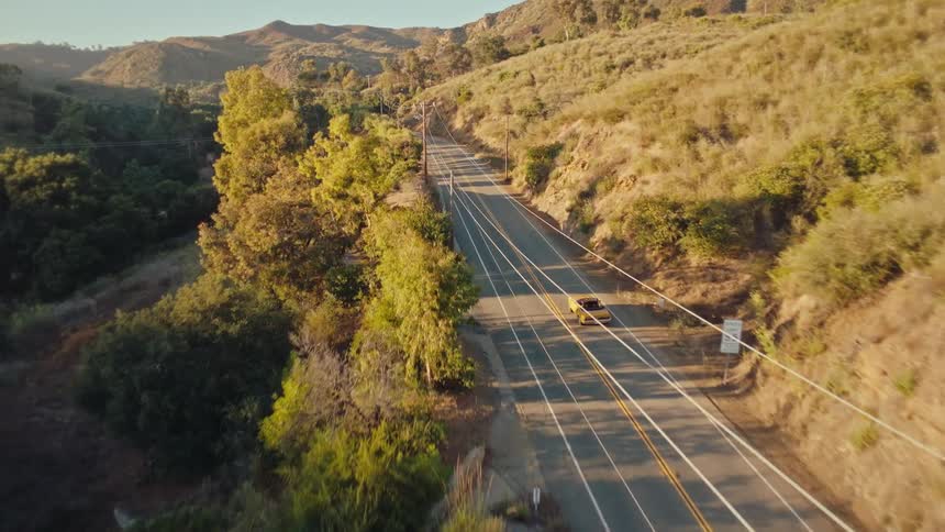 Classic car traveling on a highway surrounded by forested mountains