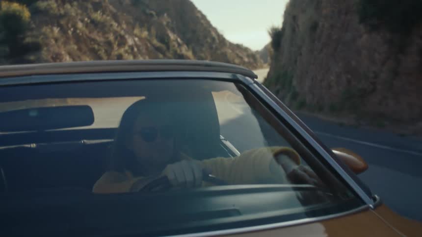 Man in sunglasses driving and traveling down a road with a convertible car