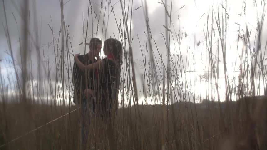 Two people embrace on a field on a cloudy day
