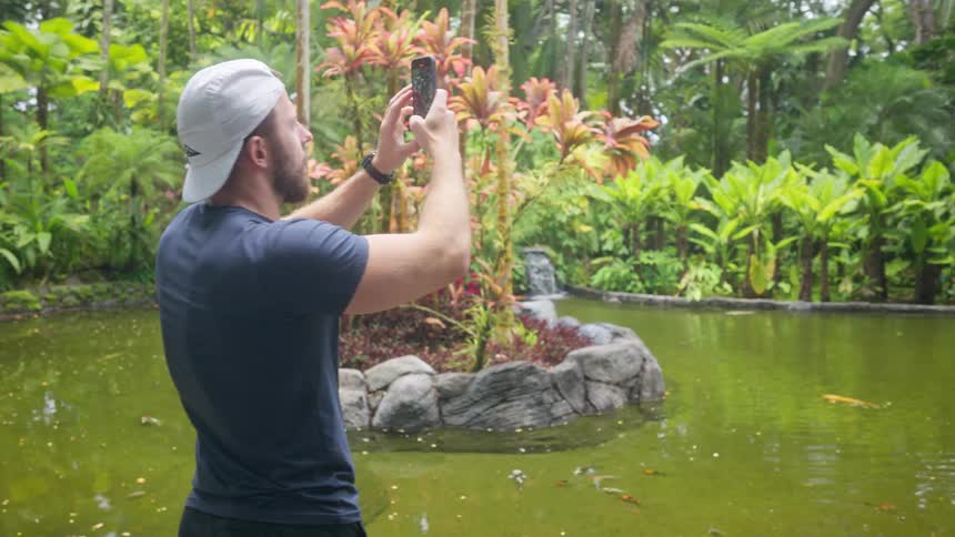 Man taking pictures in a natural park in front of a lake surrounded by vegetation