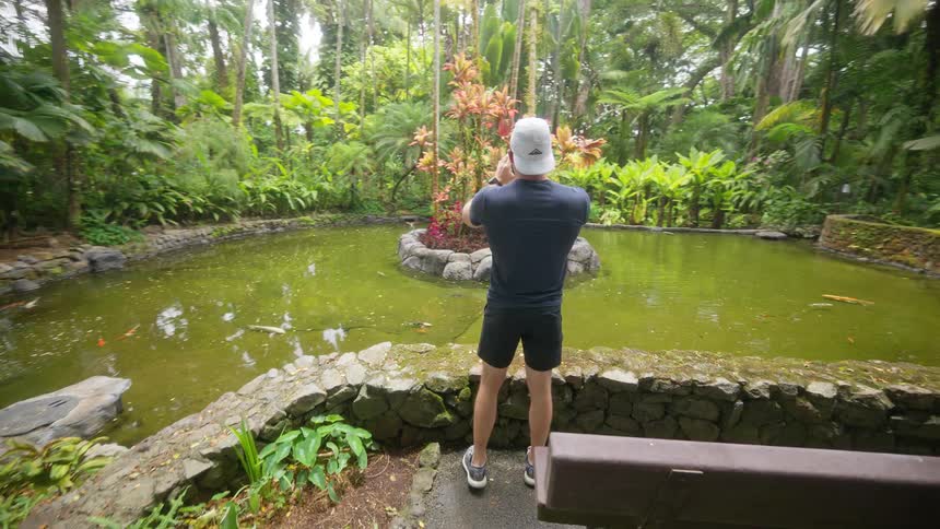 A man is video recording a lush jungle area with a mossy fountain area