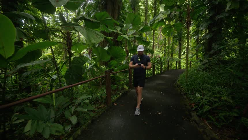 Man in a cap walking along a trail in a park surrounded by green vegetation