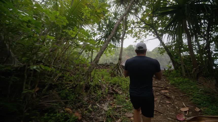 Man photographing the sea on a coastal trail surrounded by vegetation