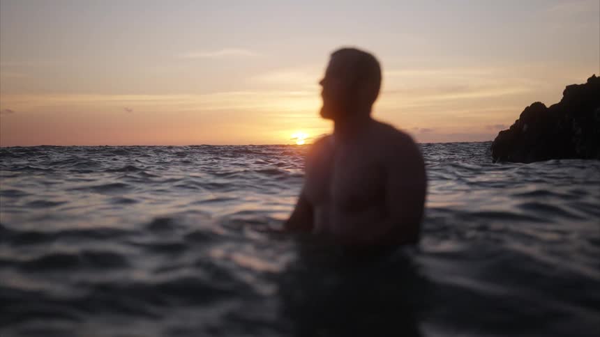Man in the sea at sunset with a partially blurred silhouette