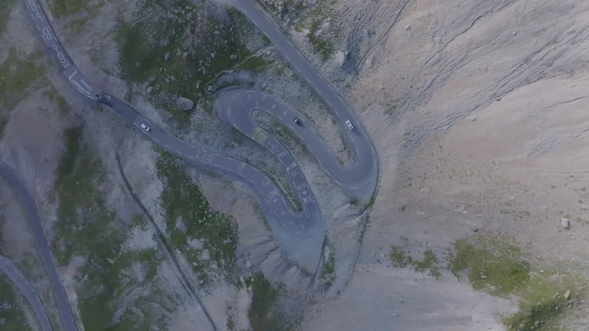 An aerial view looks down on cars driving along a winding mountain road with tight switchbacks