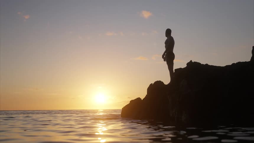 A man stands on the rocks by the edge of the ocean