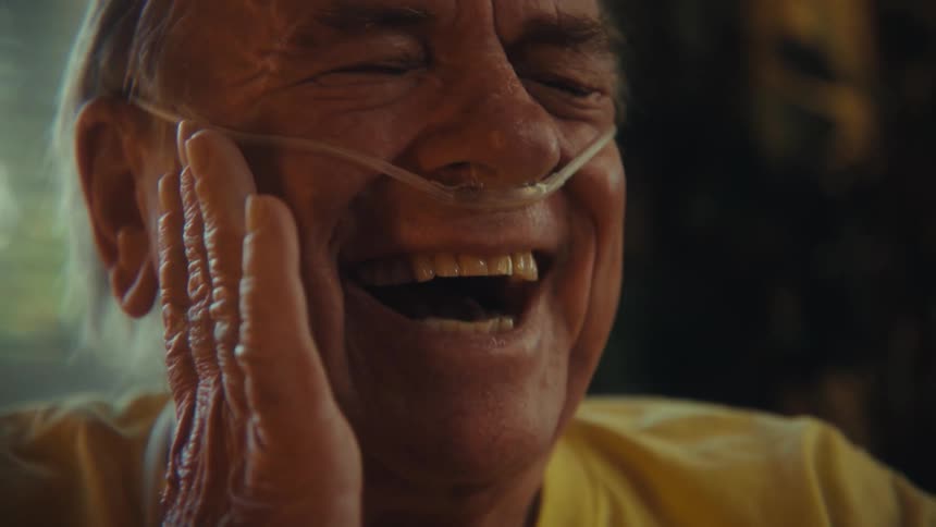 Elderly man laughing while watching on smartphone