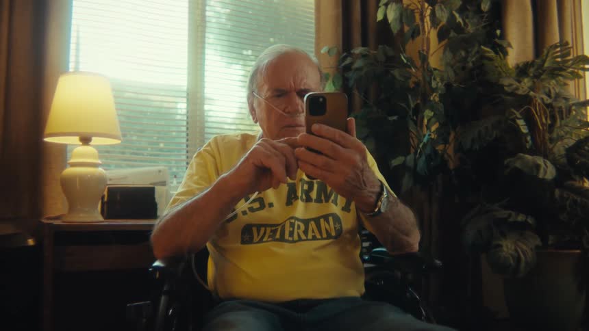 An elderly man is sitting in an armchair while scrolling on the smartphone