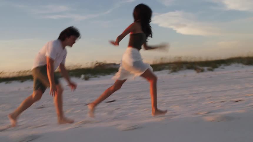 Woman and a man running on the beach sand in the late afternoon