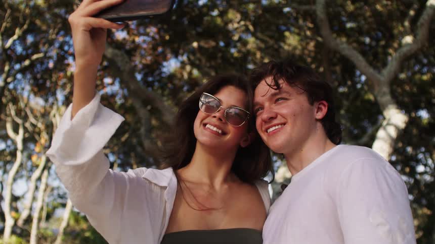 Smiling couple under a tree taking a selfie