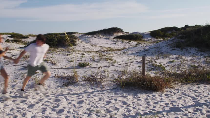 Couple running hand in hand through a sandy area with vegetation