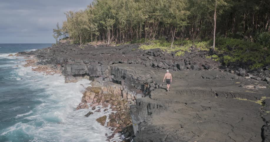 Shirtless man walking on rocky shore by the sea