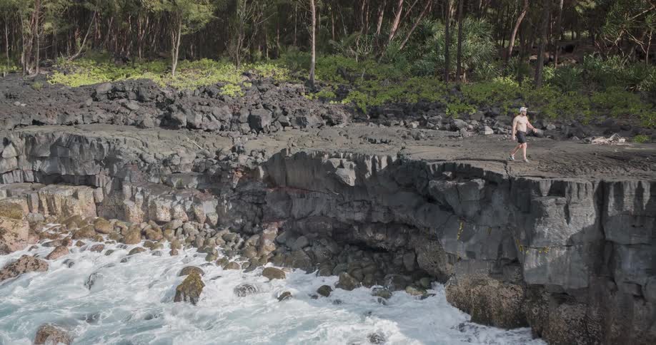 Man walking along the edge of a cliff as waves crash into the rocks below