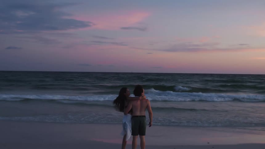 The video shows a man and a woman in a boat on a body of water with a beautiful landscape in the background they are leaning back and enjoying the moment with the camera focused on them