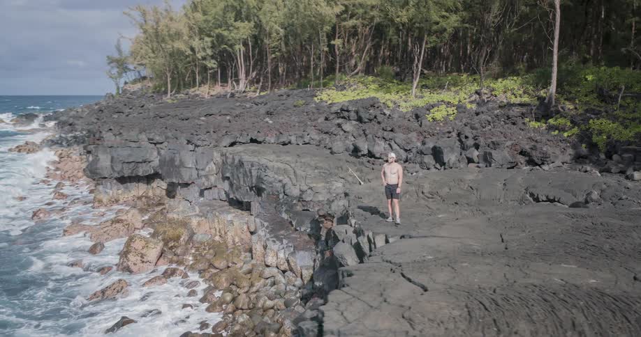 Man with hand on hip and shirtless on a cliff by the sea