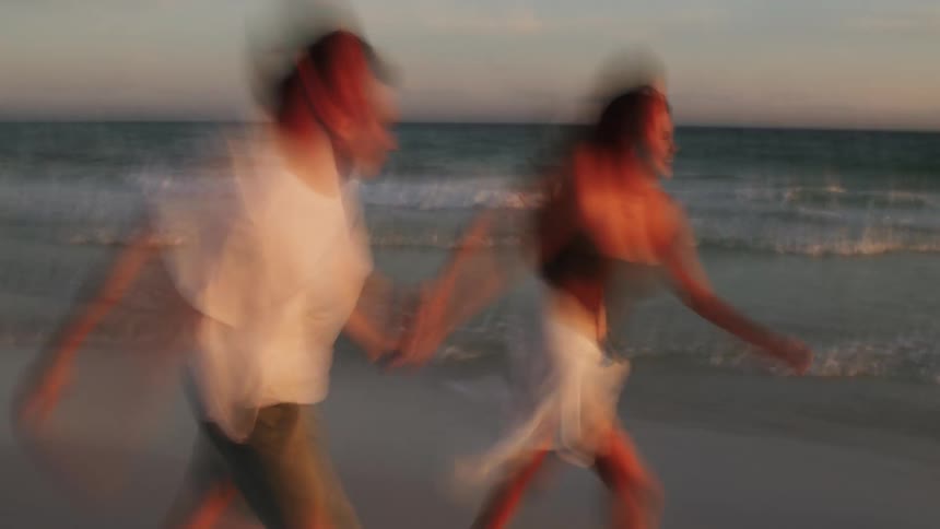 A young couple playing and holding hands on the beach at midday