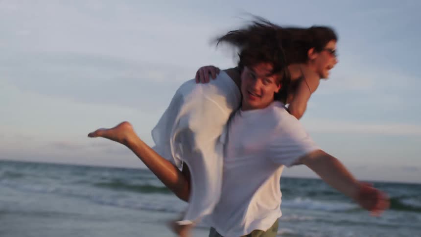 A couple having fun on the beach as the man picks up the young woman on his shoulders running on the beach sand at midday