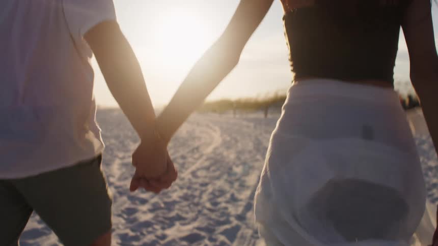 Couple walking hand in hand on the beach sand in the late afternoon
