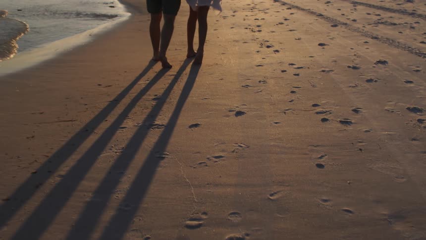 Couple walking arm in arm on the beach at sunset
