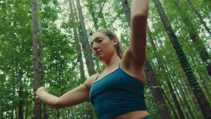 A young woman performs stretching exercises on a wooden deck in a forest