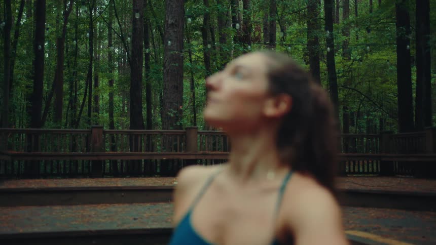 A woman stretches outdoors in a forest while looking upward