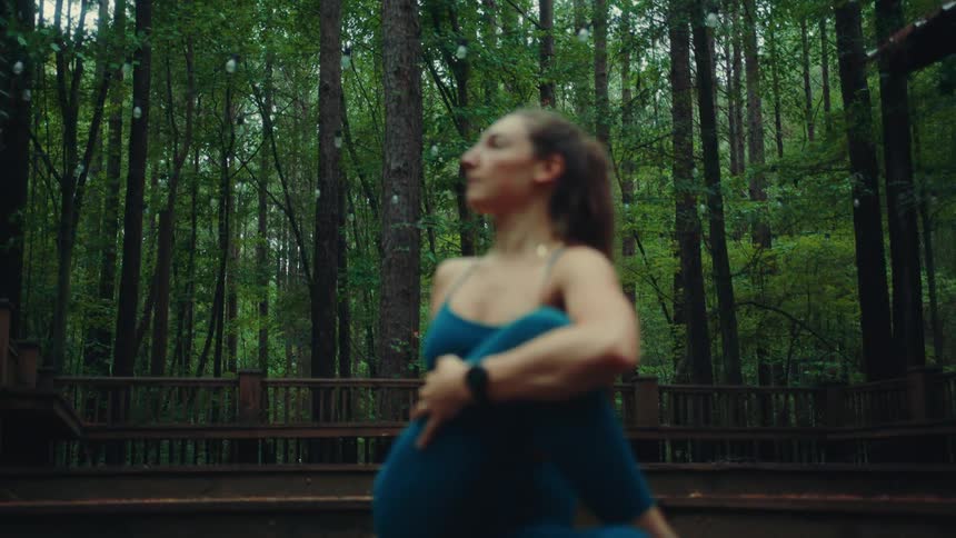 Woman in blue sportswear stretches on a deck surrounded by trees
