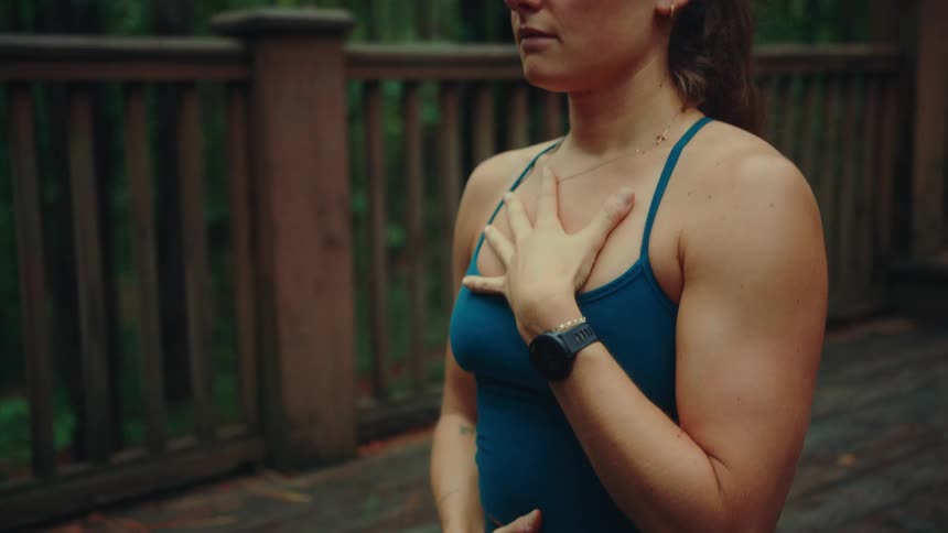 Woman in blue sportswear holds her belly and chest while exercising on a wooden deck