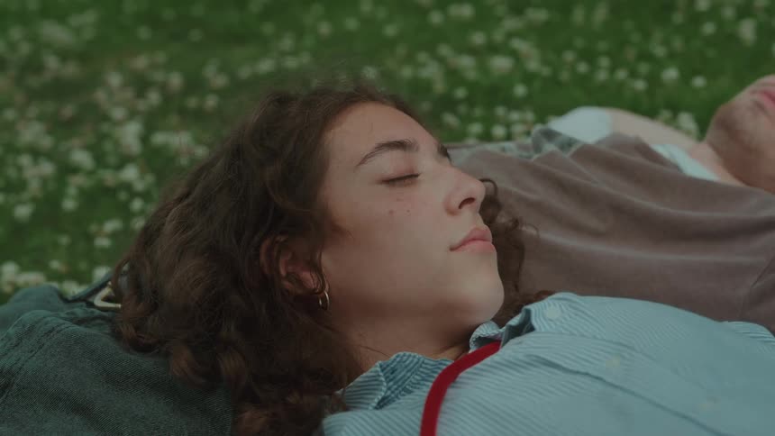 Woman lying on the grass with eyes closed next to another person
