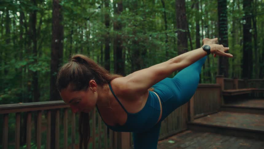 Woman practicing yoga outdoors on a wooden platform surrounded by trees