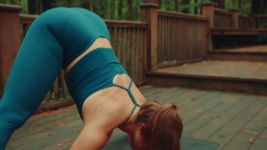 A woman doing yoga outdoors bends downward to touch her head to the ground