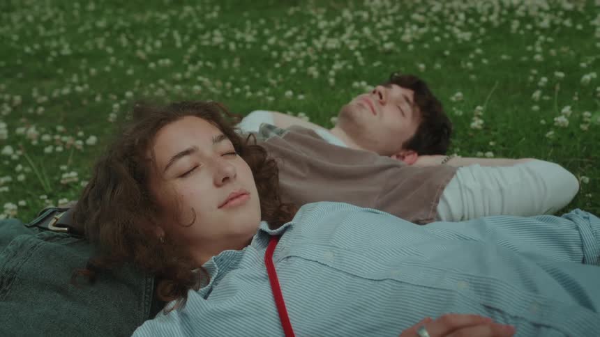 Young couple laying on a meadow covered in small flowers sleeping