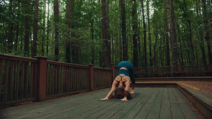 A woman performs yoga stretches on a deck surrounded by forest