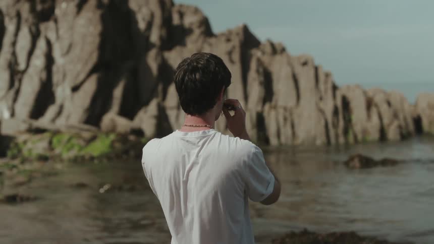 Young man laughing and playing around with seaweed moustache on his face as he stands along the coast