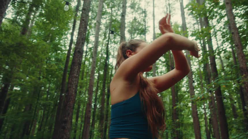 Woman in blue sportswear performs an arm stretching movement in the middle of a forest