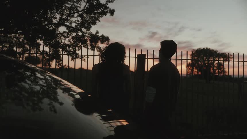 Silhouettes of two people watching the sunset behind a metal fence