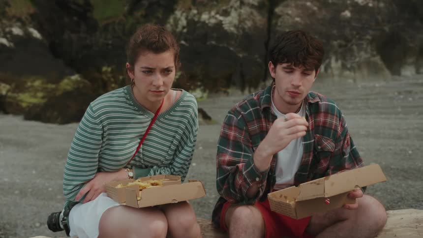 Woman and man sitting on the beach eating fries from cardboard boxes