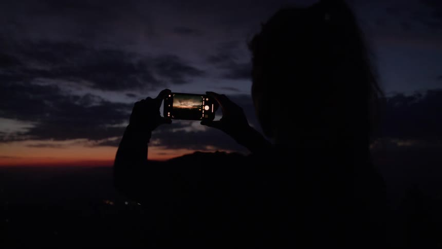 Silhouette of a person photographing the sunset with a phone