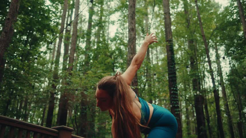 Woman practicing a yoga pose on a wooden deck surrounded by trees