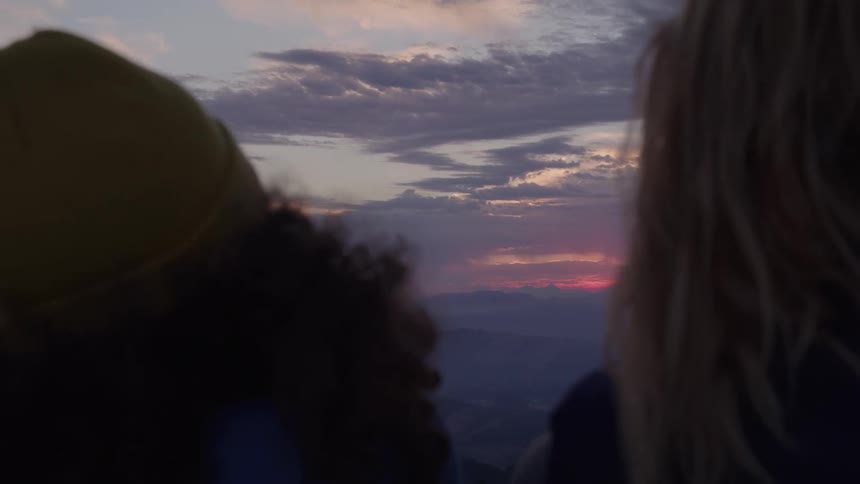 Two people watch the horizon painted with clouds at sunset