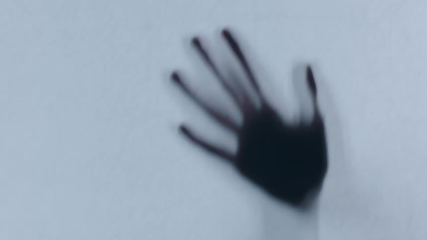 A silhouetted hand with long splayed fingers suddenly appear on a light gray textured background
