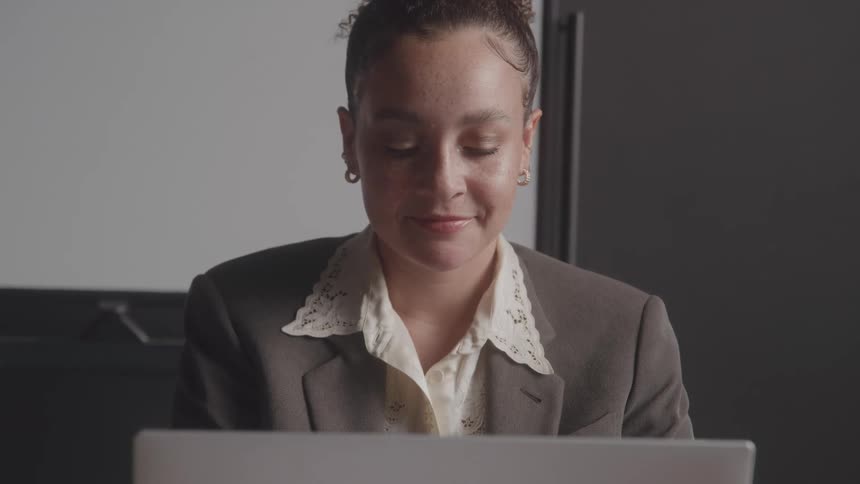 A woman wearing a blazer suit works on a laptop in her office at midday