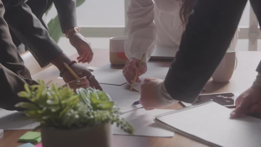 Group of people with pens and pencils interacting at an office desk